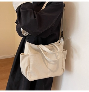 Model wearing a large cream corduroy tote bag with side pockets and detachable strap