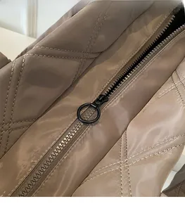 Detail of metal circular zipper pull and diamond quilted stitching on brown tote bag