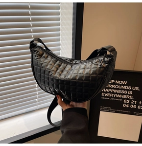 Detailed view of black quilted puffer crossbody bag with crescent shape and strap