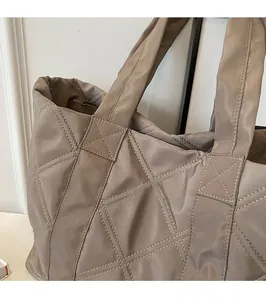 Detail of reinforced cross-stitching on brown quilted nylon tote bag shoulder straps