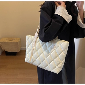 Detail einer beigen gesteppten Nylon-Einkaufstasche, getragen von einem Model im Raum