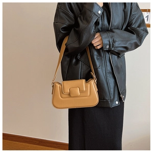 Detail view of a light brown minimalist PU leather underarm bag worn over a black jacket