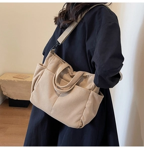 Detailed close-up of beige corduroy tote bag with multiple pockets and black hardware