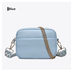 Detail of light blue pebble leather camera bag with wide geometric strap and gold hardware