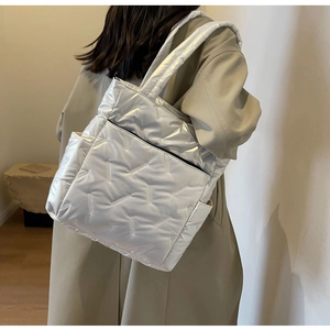 Silver metallic quilted tote bag with dual straps shown on a model in a minimal interior