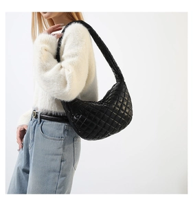 Side view of a black quilted cloud shoulder bag worn by a model in a white sweater