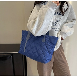 Detail der blau gesteppten Nylon-Tragetasche mit gepolsterter Textur und praktischen Tragegriffen