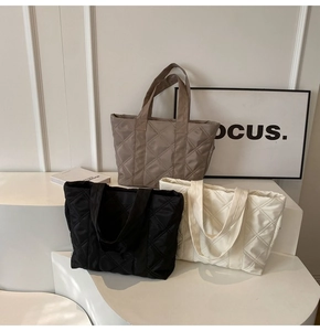 Three minimalist quilted nylon tote bags in black, white, and khaki on a clean tiered display