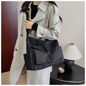 Detail of a black canvas crossbody bag with multiple pockets and wide strap on a model
