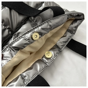 Detail of silver quilted puffer bag with magnetic closure and durable black canvas handles