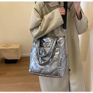 Silver quilted crossbody tote bag shown on a model with long trench coat for size scale