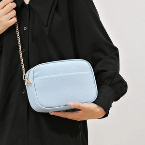 Sac bandoulière bleu clair à grain litchi avec chaîne dorée porté par un modèle
