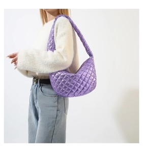 Detailed view of purple metallic quilted shoulder bag worn by model over a white sweater