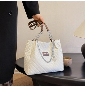 Détail d'un cabas blanc matelassé avec chaîne argentée et poignée en cuir marron
