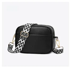 Detail of black pebbled leather crossbody bag with geometric wide strap and gold hardware