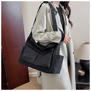 Detail of black canvas messenger bag with large front pockets and adjustable strap