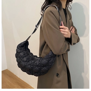 Dettaglio di una borsa hobo trapuntata nera con tracolla a righe e tessuto in nylon