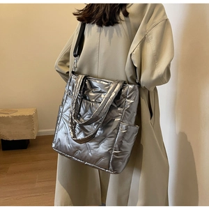 Detail view of quilted metallic tote bag featuring silver texture and wide black strap