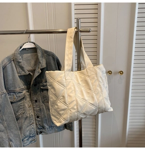 Detail of cream quilted tote bag with diamond pattern hanging on a metal hanger