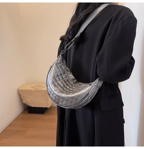 Detail view of a silver metallic quilted half-moon crossbody bag on a black blazer