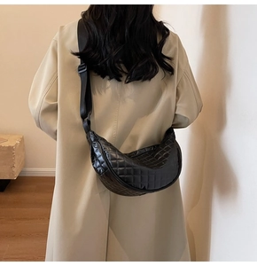 Detailed back view of a black quilted crescent crossbody bag worn over a beige trench coat