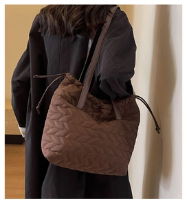 Detail of a dark brown quilted shoulder bag with drawstring closure on a black coat