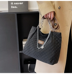 Détail du sac bandoulière en nylon matelassé noir avec patch en cuir brun et chaîne dorée