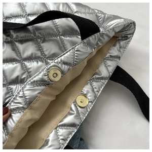 Detail of silver metallic quilted handbag featuring a gold magnetic closure and beige lining