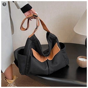 Detail of black canvas tote bag showing brown leather strap and side pocket design