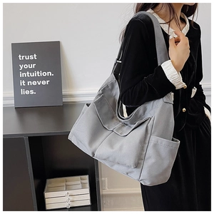 Detailed view of the grey canvas tote bag with multi-pocket utility design and wide black strap