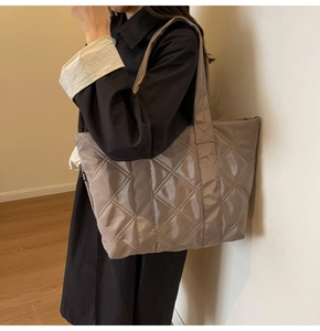 Detailed side view of khaki quilted shoulder bag with glossy nylon finish on a model