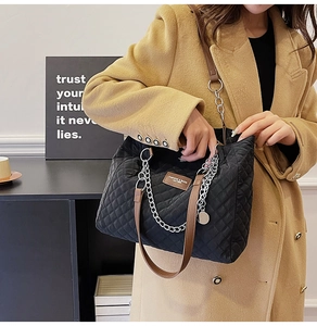 Détail du sac cabas matelassé noir avec chaîne argentée et poignée en cuir sur un modèle