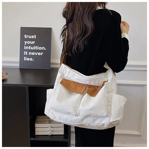 Detail of adjustable brown strap and double front utility pockets on white canvas bag