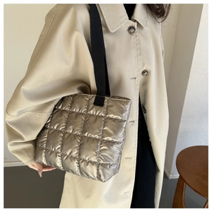 Close-up of a metallic silver quilted tote bag with black canvas shoulder straps on model