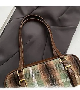 Close-up of brown leather straps and gold metal buckles on a wool plaid shoulder bag