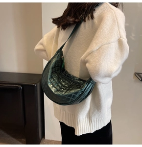 Detail view of dark green quilted half-moon crossbody bag on white sweater