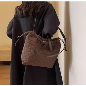 Detail of a brown quilted tote bag showing leaf-vein stitching on a models shoulder