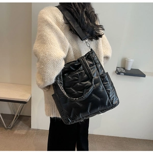 Rear view of model wearing a black quilted puffer crossbody bag with a wide nylon strap