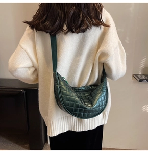 Detail of dark green quilted half-moon crossbody bag with wide shoulder strap on model