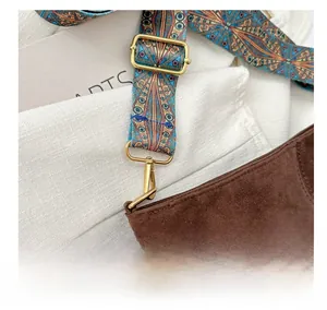 Detailed close-up of brown suede bag featuring bohemian floral strap and gold metal hooks