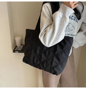 Shoulder shot of a black quilted tote bag with diamond texture and wide strap