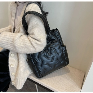 Detail of black quilted puffer tote bag with glossy finish on shoulder of female model