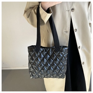 Detail view of black quilted down handbag with glossy nylon material and woven straps