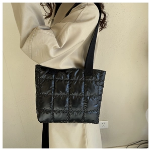 Detail of black quilted nylon tote bag with rhombus stitching and woven strap on model