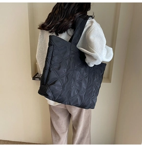 Close-up of a large black quilted tote bag with wide strap worn over a shoulder