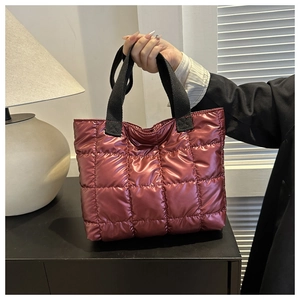 Detailed view of burgundy quilted puffer handbag with glossy finish and wide black handles