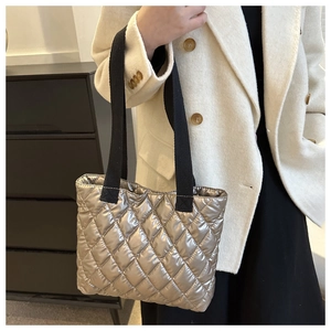 Detail of silver quilted tote bag featuring metallic finish and black woven strap on model
