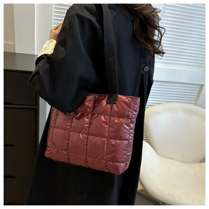 Macro shot of burgundy quilted down tote bag with shiny nylon finish and black strap
