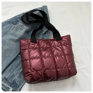 Close-up of wine red quilted tote bag with black straps on denim jacket background