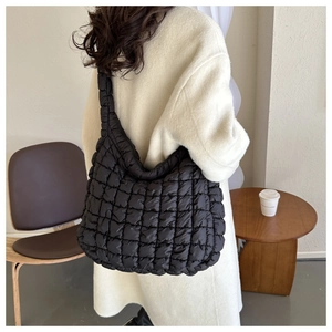 Gros plan d'un sac cabas noir matelassé avec une large bandoulière porté par un mannequin